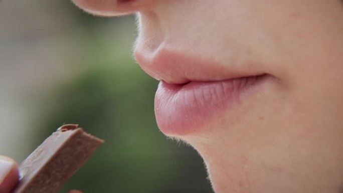 特写性感粉色女性嘴唇满意地咬着甜巧克力棒