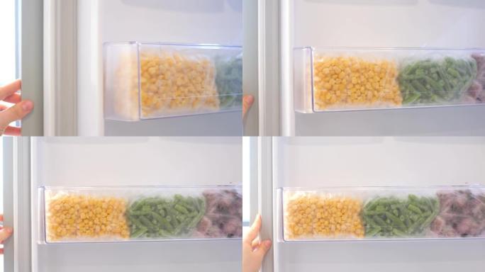 女性的手打开冰箱，冰箱中的冷冻蔬菜包装在架子上。