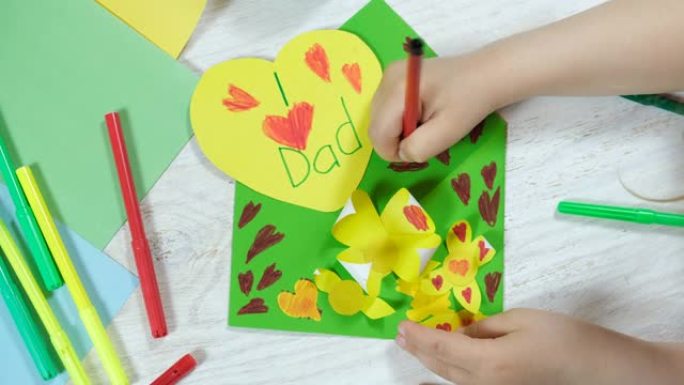 小女孩为爸爸准备了一个惊喜。父亲节贺卡心。信封工艺品和彩纸上的花。手工制作。DIY概念。