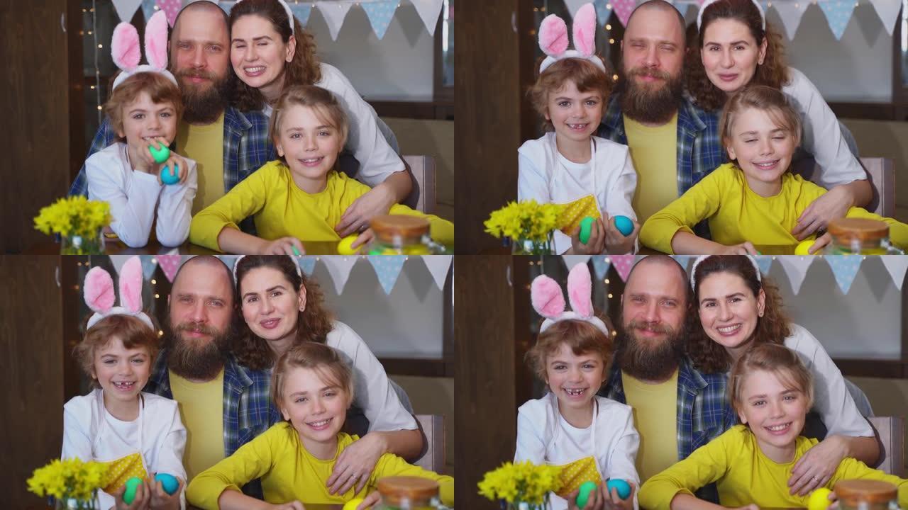 复活节周日家庭传统。父母爸爸妈妈两个白种人快乐的孩子，兔子耳朵摆姿势微笑着看着复活节装饰的鸡蛋的相机