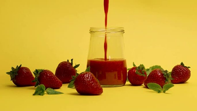 将红色草莓冰沙倒入装有稻草和散落的浆果的玻璃罐中，这些浆果被隔离在黄色背景上。特写。健康的概念。排毒