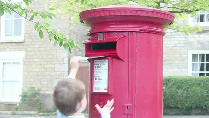 小男孩在红色邮箱里寄信