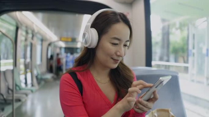 亚洲女性在地铁列车中使用智能手机，在耳机中听音乐音乐应用程序找到最喜欢的配乐歌手歌曲