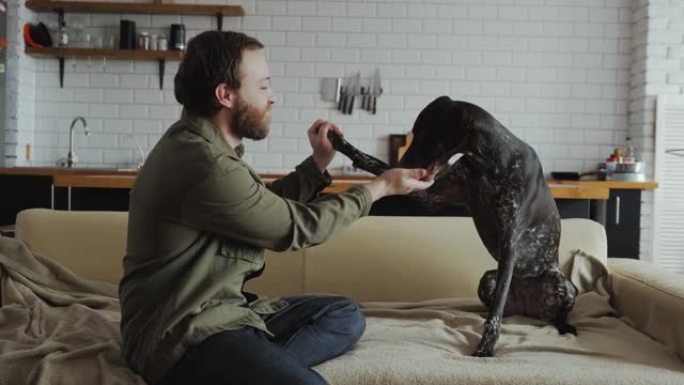 一个男人和他的狗坐在家里的沙发上，训练她到高五
