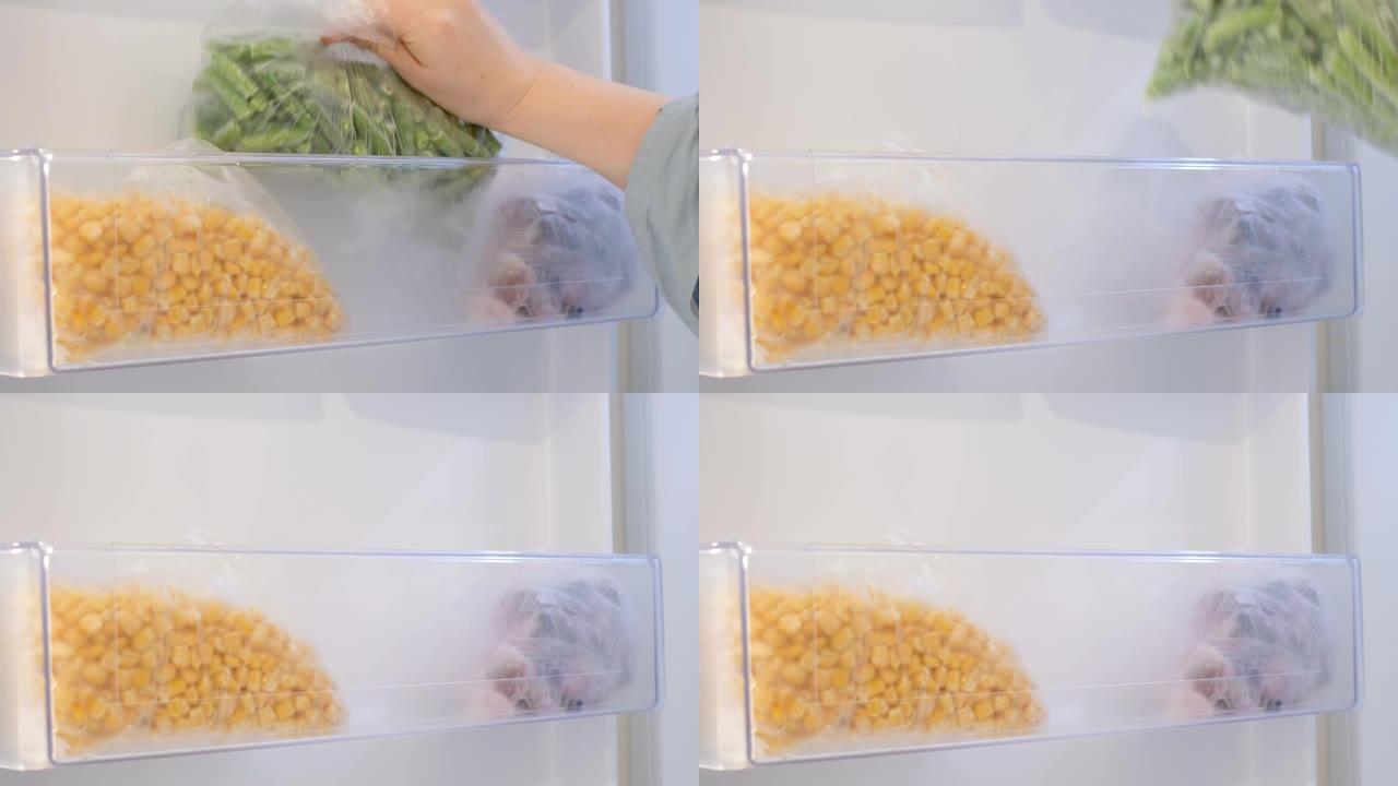 女性的手从冰箱中拉出塑料袋中的冷冻蔬菜。