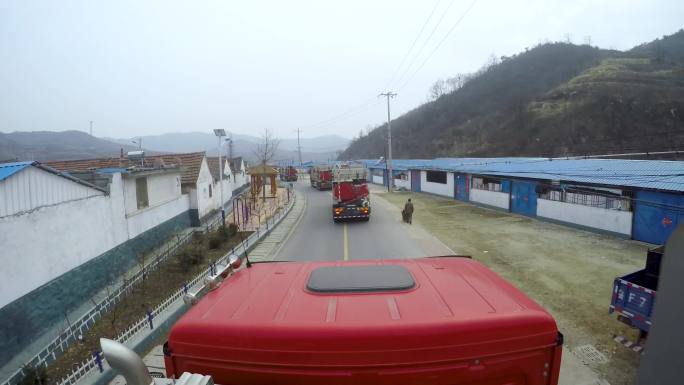 一辆卡车在路上行驶 多辆卡车在工厂准备出发 一个穿橙色工作服的男人正在驾驶卡车