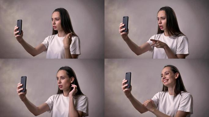 年轻的黑发女孩在智能手机上进行视频通话，交流概念，灰色背景