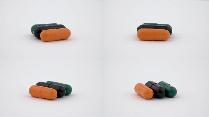 三个硬淀粉胶囊在转盘上旋转。橙色、黑色和绿色。孤立在白色背景上。特写宏。