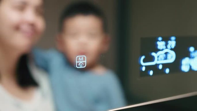 开朗的亚洲妇女抱着儿子在房子里调节和控制灯光。家庭自动化和智能家居技术。