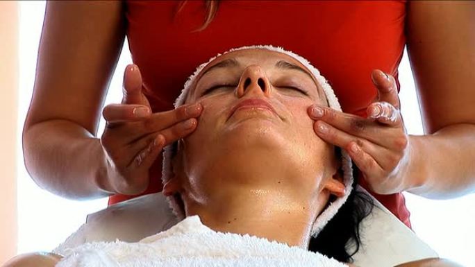 迷人的黑发女人从美丽的金发治疗师那里得到面部按摩