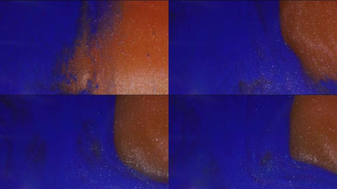 橙色和蓝色闪光涂料在水中旋转和混合背景