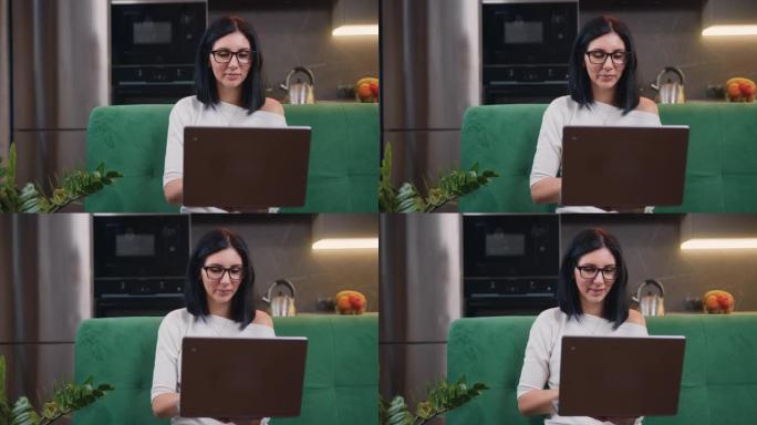 坐在绿色沙发上的迷人的沉思黑发女人的特写镜头在笔记本电脑上远程工作，在家做自由职业在线工作。工作流概
