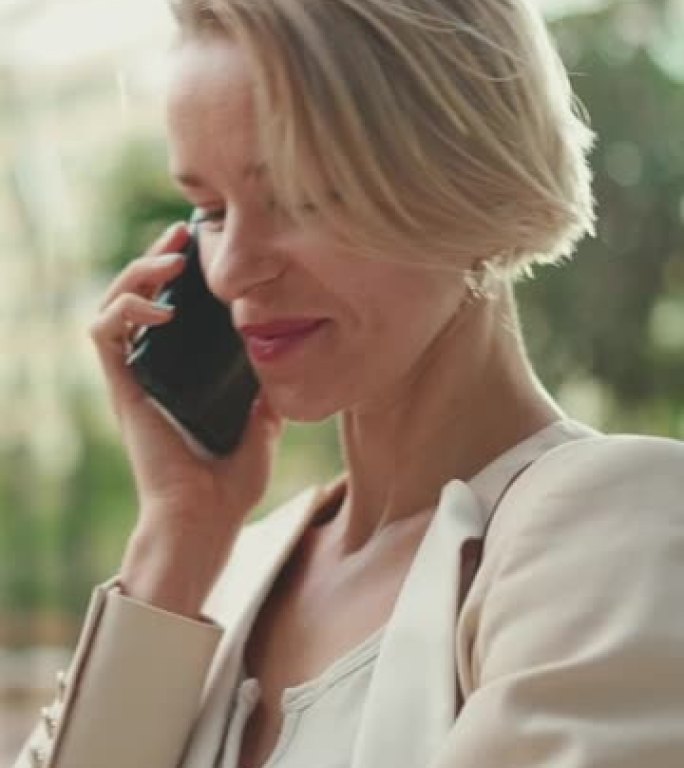 垂直视频: 金发碧眼的快乐女商人在手机上聊天，划算，成功