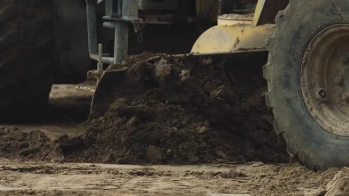 挖掘机挖入污垢并将其扔到容器中的污垢堆上