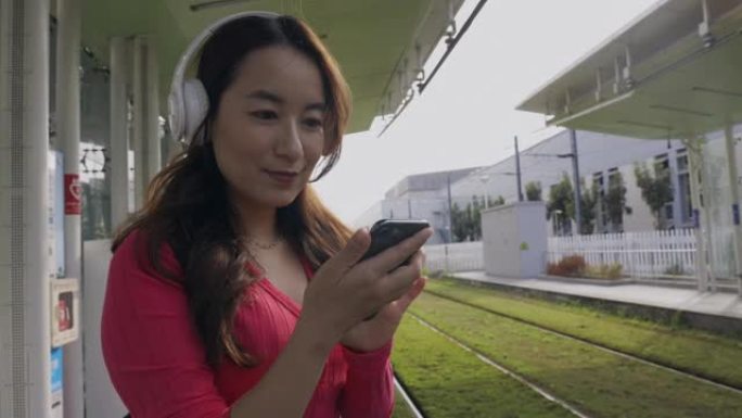 在城市中行走的亚洲女性使用智能手机在耳机中听音乐进行音乐应用，在户外寻找最喜欢的配乐歌手歌曲