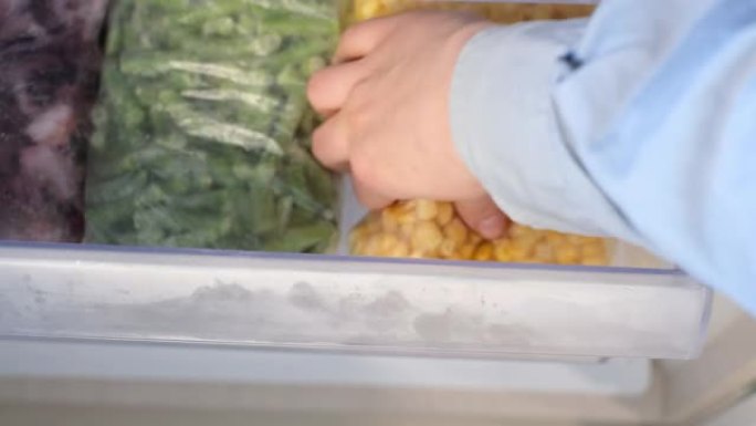 女性手打开冰箱中冷冻食品的架子特写顶视图。