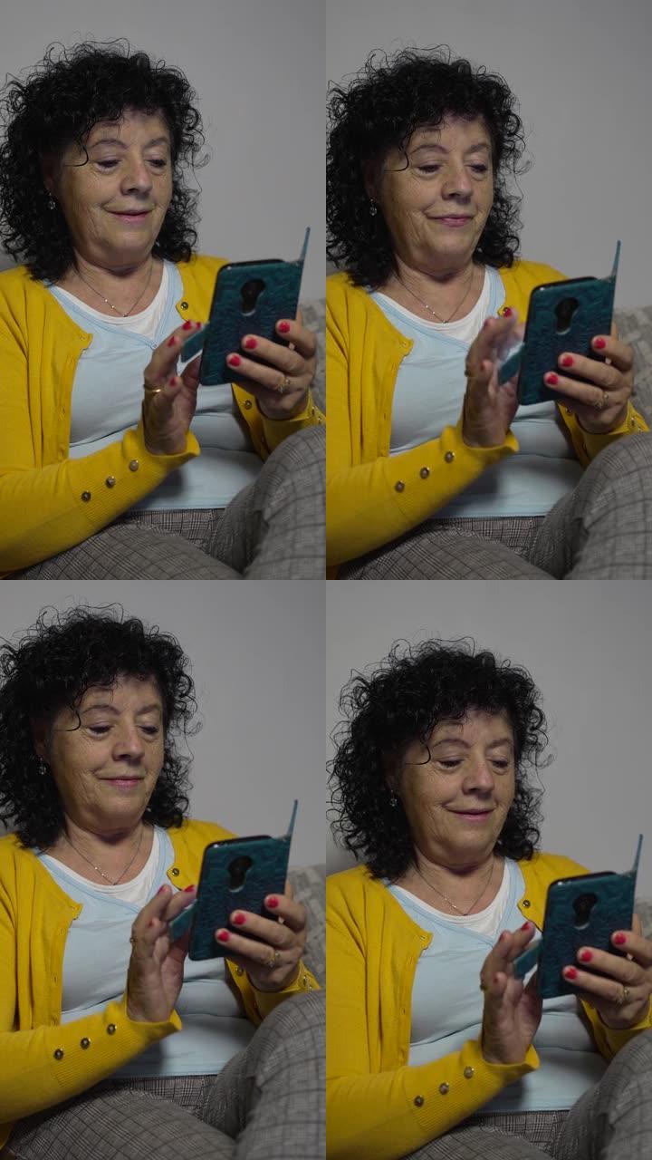 一个穿着黄色毛衣的老妇人坐在客厅沙发上，一边看着并操纵着她的带书皮的手机的垂直视频。