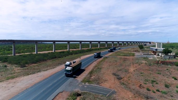 种满绿植的土地上有一条公路 装满货物的货车在公路上行驶 卡车在高架桥和高速上行驶