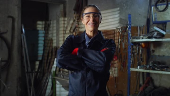 年轻女机械师的肖像，穿着制服工作服和护目镜看着相机和微笑在她的车间。职业自信的焊工，挑战刻板印象
