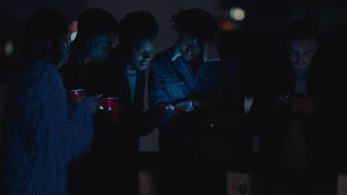 一群朋友晚上在屋顶上放松，使用智能手机技术发短信分享社交媒体生活方式在线浏览，享受周末聚会