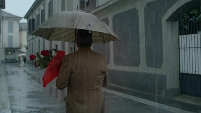 背景图: 中年男子在雨下走在街上，拿着雨伞和红玫瑰花束。高级男子回家与妻子庆祝情人节，送花