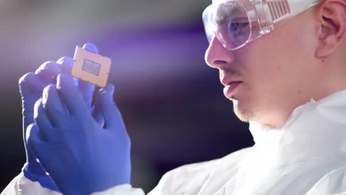 未来技术概念: 一名穿着无菌工作服的工程师戴着手套拿着一个电脑微芯片，并对其进行检查。CPU处理器的