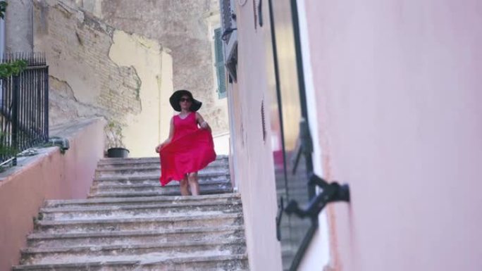 希腊科孚岛的旅游妇女。穿着红色连衣裙的快乐优雅时尚模特在希腊克罗夫岛的老城区著名地标享受假期，慢动作