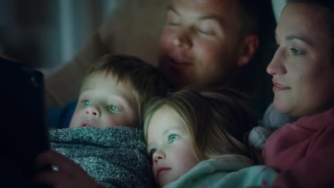 幸福的家庭使用平板电脑和孩子母亲和父亲享受与孩子一起看娱乐触摸屏技术睡觉前放松