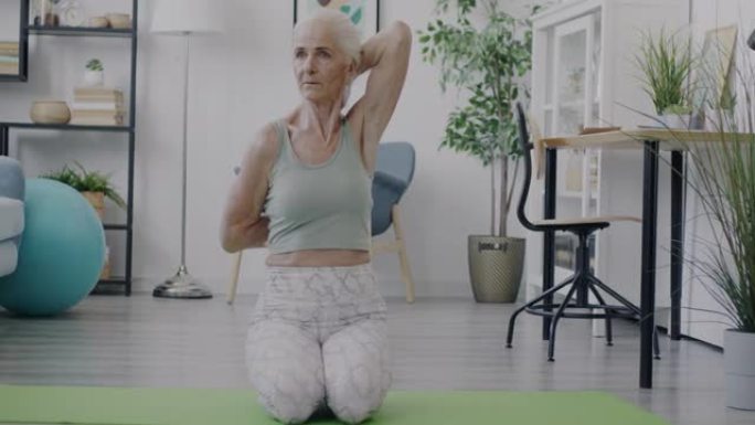 放松的高级女性做瑜伽伸展手臂在家享受个人练习的慢动作肖像