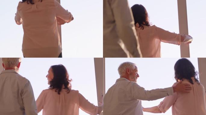 幸福的夫妇拥抱在家里，看着日落时的窗外，享受成功的退休生活方式，分享浪漫的联系