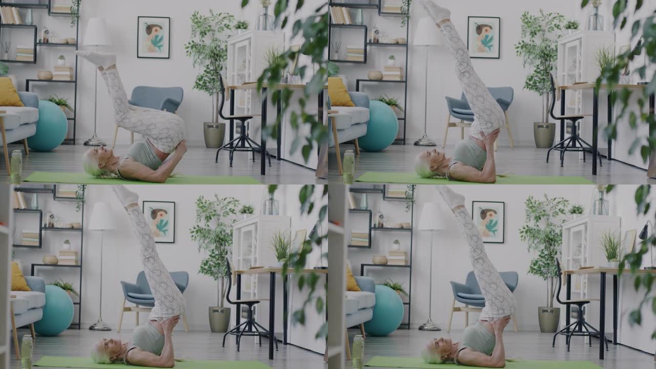 侧视图灵活的年长的妇女做瑜伽体式躺在垫子上和提高腿享受练习在家