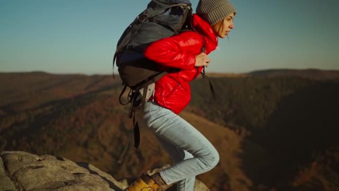 慢镜头的冒险女徒步旅行者，穿着红色夹克，背着背包，坐在日落时分的悬崖顶上，休息后站起来准备出发。再接