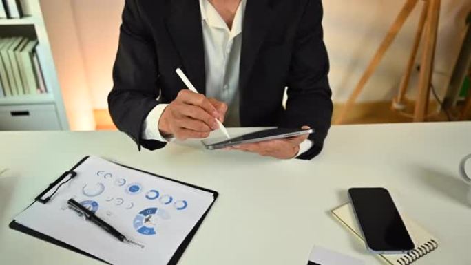 男性专业企业家使用手写笔在数字平板电脑上书写，坐在工作场所管理任务。