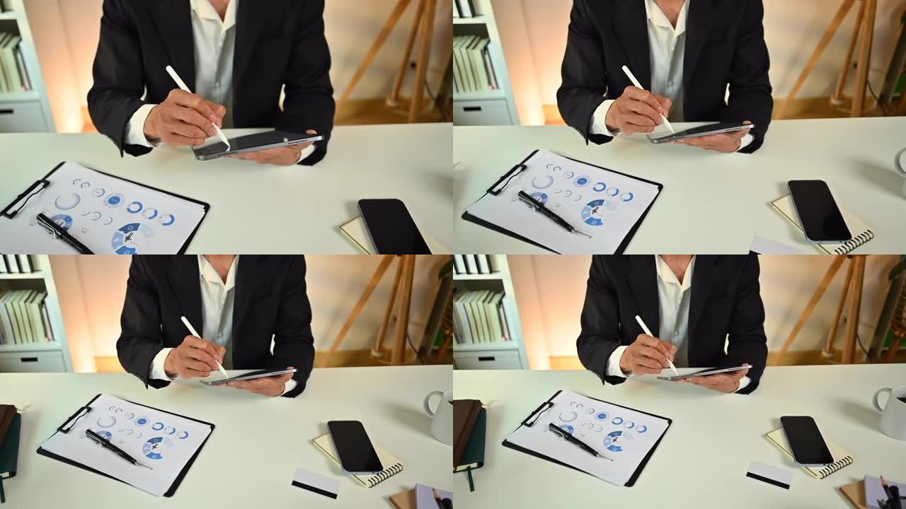男性专业企业家使用手写笔在数字平板电脑上书写，坐在工作场所管理任务。