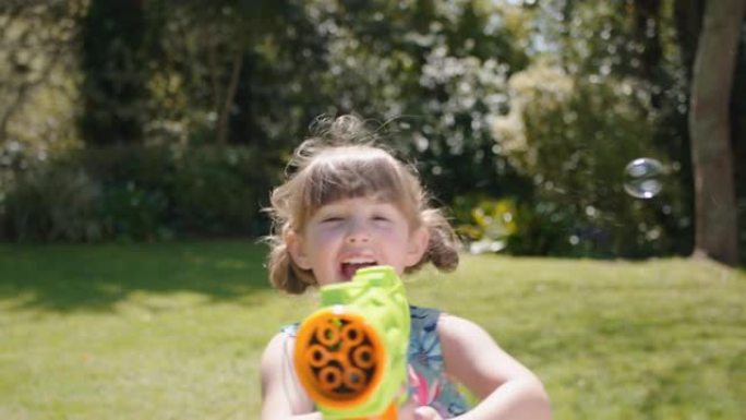 快乐的小女孩吹肥皂泡在阳光明媚的花园里玩玩具枪享受有趣的游戏有趣的顽皮的孩子享受夏天4k