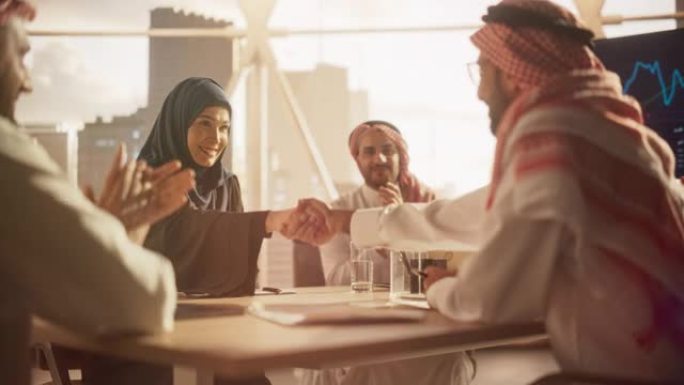 穆斯林商人在公司现代办公室完成业务交易。男女代表握手，庆祝成功的伙伴关系。沙特，阿联酋，阿拉伯办公室