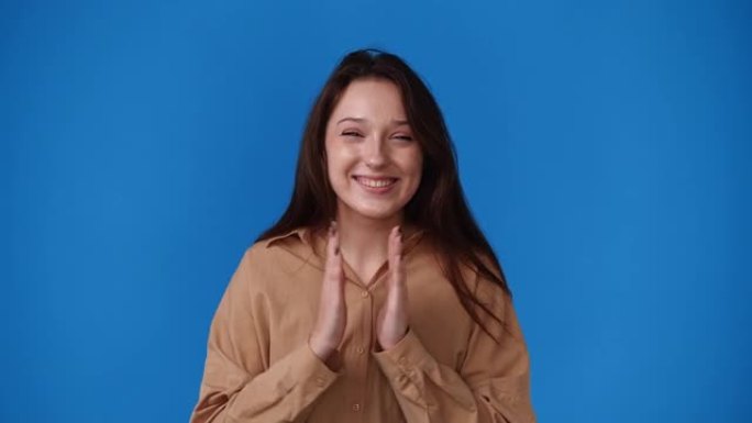 一个女孩拍手并在蓝色背景上微笑的4k视频。