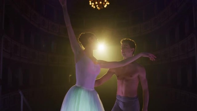 两名年轻的古典芭蕾舞演员在经典剧院的舞台上表演的电影镜头，并带有戏剧性的灯光。专业男女表演者优雅地排
