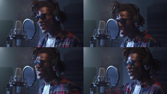 用耳机在专业录音室录制专辑的年轻黑人男性歌手的特写肖像。富有表现力的年轻人带着情感唱歌，开始了成功的