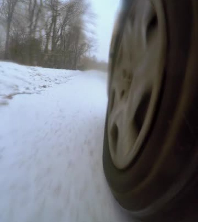 特写车轮从汽车视点下旋转。在雪地冬季道路上驾驶汽车垂直视频