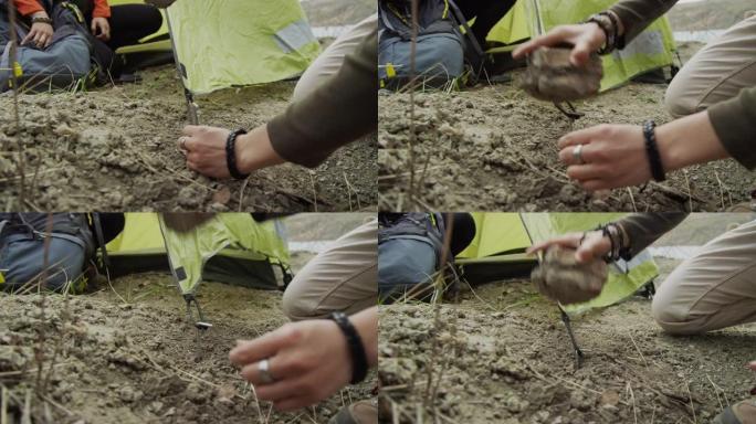 两个朋友在海岸徒步旅行的特写镜头，双手用岩石加固帐篷杆