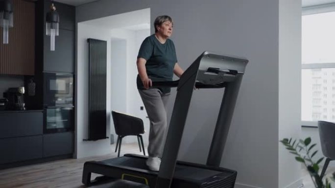 现代公寓客厅跑步机上的成熟女性，老年健康生活方式