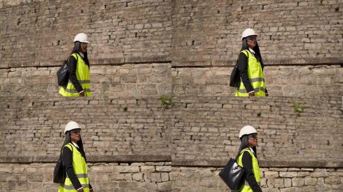 在城市环境中，穿着背心，防护眼镜和安全帽头盔的女工程师侦察施工现场。