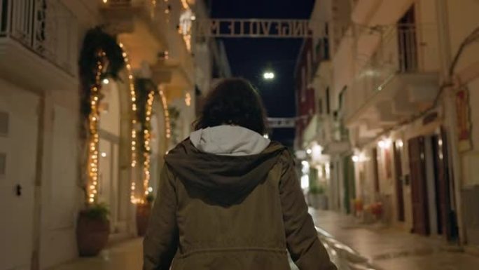 年轻女孩晚上在意大利的街道上散步。她欢欣鼓舞，举起双手。