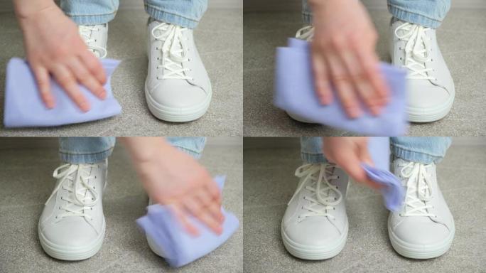 一名妇女用抹布清洁白色皮革运动鞋，清除灰尘，向前迈出一步