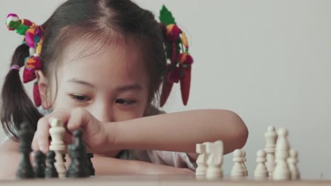 可爱的亚洲小女孩在明亮的白色房间里玩棋盘游戏，阳光普照，展示了战略规划、创造力和儿童教育决策的概念。