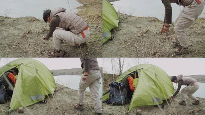 两名亚洲女性游客在多风的岩石湖海岸搭起帐篷