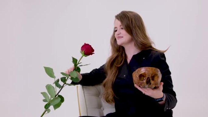 一个黑衣女人一只手拿着一朵红玫瑰另一只手一个人的头骨阴险的女人吸血鬼华丽的头发在白色背景上失去了爱情