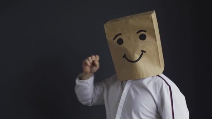 一个头上装着纸袋的男人，脸上画着笑脸，正在跳舞。