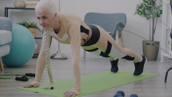 穿着运动服的老年妇女独自在家锻炼木板姿势